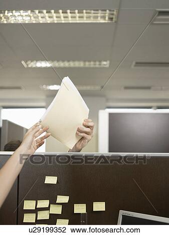 Stock Image - Office workers passing files over partition wall (close-up). Fotosearch