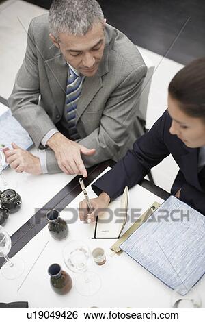 Two businesspeople making notes at dining table (high angle view) View Large Photo Image Stock Photograph - Two businesspeople making notes at dining table (high angle view). Fotosearch