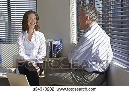 Stock Image - Two Businesspeople Talking by Window. Fotosearch
