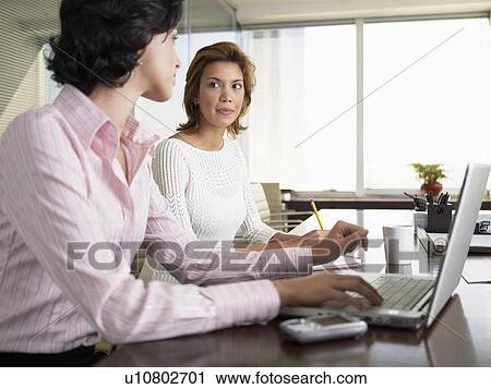 Stock Image - Two businesswomen using laptop computer in meeting. Fotosearch