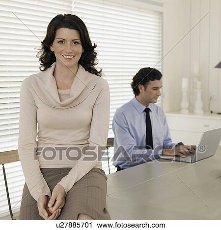 Woman sitting on table, man using laptop in background View Large Photo Image Stock Image - Woman sitting on table, man using laptop in background. Fotosearch