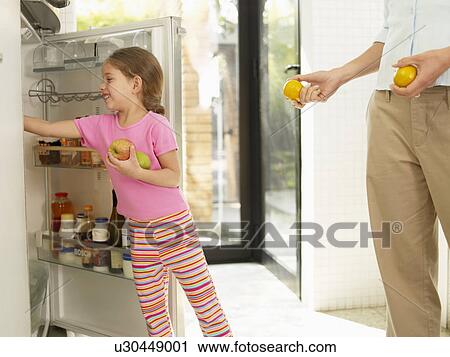 Stock Image - Girl putting fruits to fridge. Fotosearch