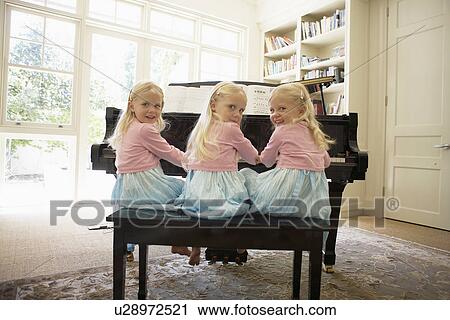 Stock Image - Triplets playing piano in living room (rear view). Fotosearch