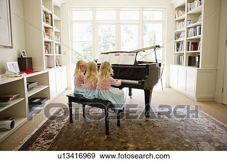 Stock Photo - Triplets playing piano in living room (rear view). Fotosearch