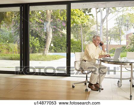 Mature man using laptop and telephone in living room View Large Photo Image Stock Image - Mature man using laptop and telephone in living room. Fotosearch
