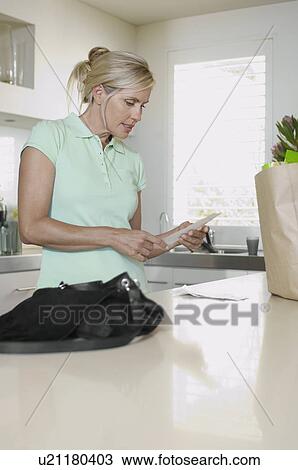 Stock Image - Mature woman checking receipts in kitchen. Fotosearch