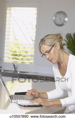Stock Image - Mature woman with diary using laptop. Fotosearch