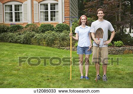 Stock Image - Young couple with rake and spade in garden. Fotosearch