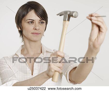 Stock Image - Young Woman Holding Hammer and Nail. Fotosearch