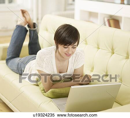 Stock Photography - Young Woman Using Laptop on Sofa. Fotosearch
