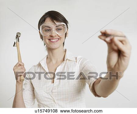 Stock Photo - Young Woman with Goggles Holding Hammer and Nail. Fotosearch