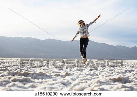 Stock Image - Mid adult woman walking with arms outstretched in desert. Fotosearch