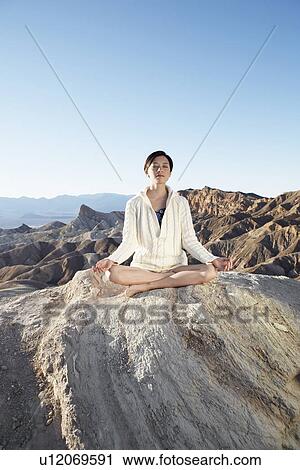 Stock Image - Woman meditating in lotus position in desert, Death Valley, California, USA. Fotosearch