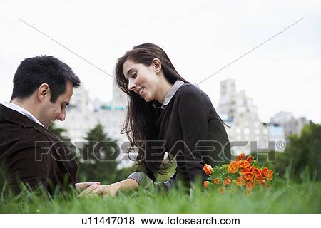 Stock Photo - Couple sitting on grass and holding hands (low angle view). Fotosearch