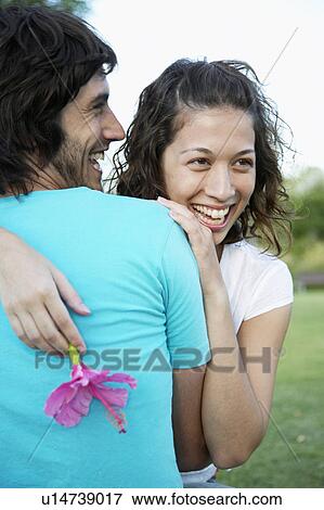 Stock Photo - Young couple hugging, woman holding flower. Fotosearch