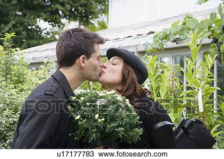 Stock Image - Young couple kissing in plant nursery. Fotosearch