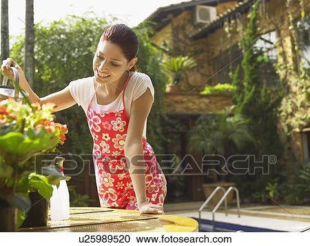 Stock Image - Young woman watering flowers. Fotosearch