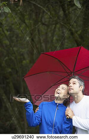 Stock Image - Couple looking at rain under umbrella. Fotosearch