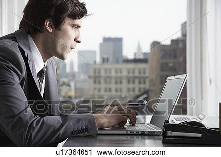 Stock Image - Businessman typing with laptop in office. Fotosearch
