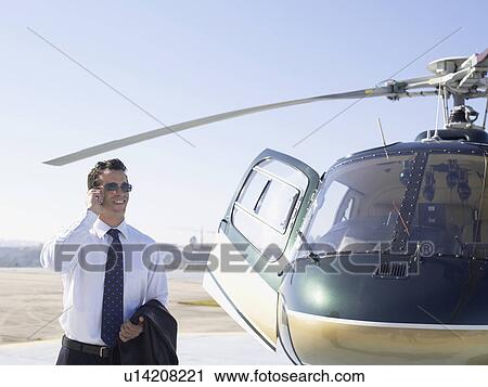 Businessman using cell phone near helicopter View Large Photo Image Stock Image - Businessman using cell phone near helicopter. Fotosearch