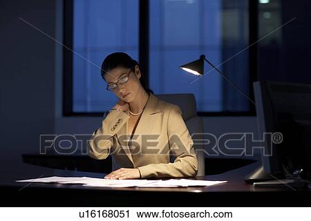 Stock Image - Female office worker working late. Fotosearch