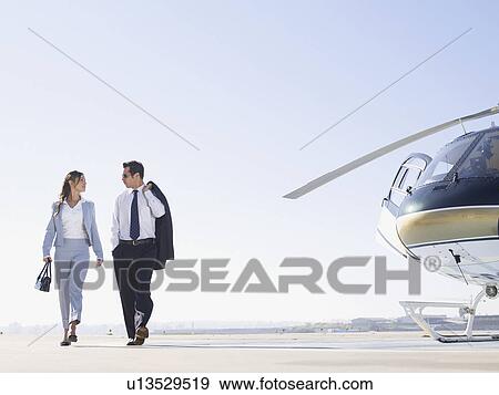 Stock Photo - Two businesspeople walking on runway near helicopter. Fotosearch