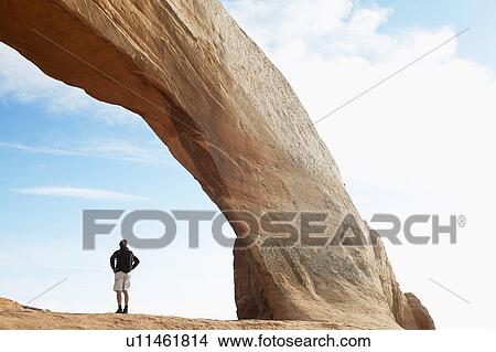 Picture - Man standing under arched rock. Fotosearch