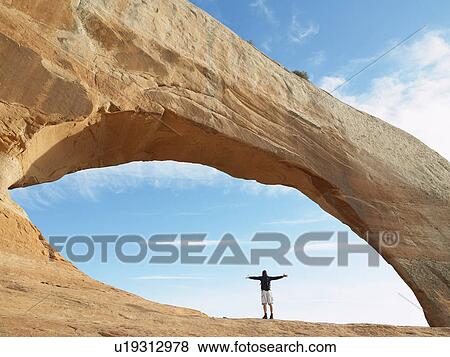 Man standing under arched rock with arms outstretched View Large Photo Image Stock Photo - Man standing under arched rock with arms outstretched. Fotosearch
