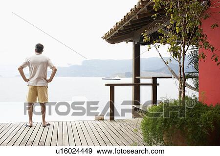 Stock Photo - Mature man looking at sea from beach hut. Fotosearch