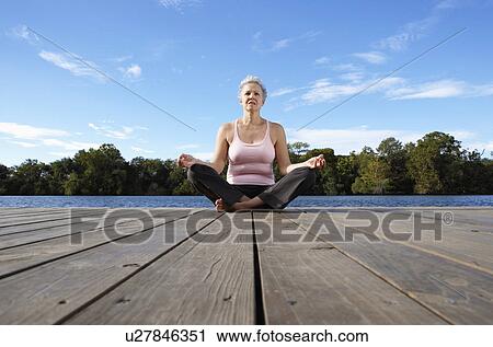 Stock Image - Mature woman meditating in lotus position (low angle view). Fotosearch