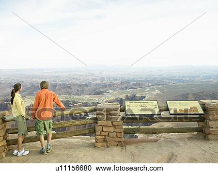 Stock Image - Tourist at observation point, rock strata in background, rear view, Moab, Utah, USA. Fotosearch