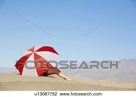 Stock Image - Woman sitting under umbrella in desert. Fotosearch