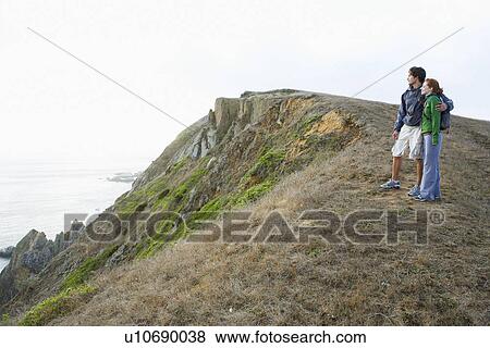 Stock Photo - Young couple looking at sea on cliff. Fotosearch