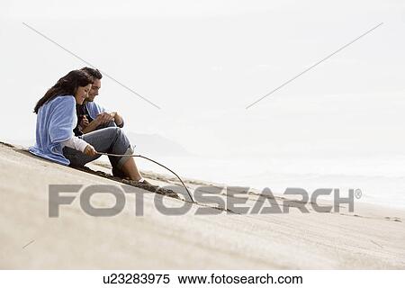 Young couple sitting on beach, woman drawing in sand with stick View Large Photo Image Stock Photography - Young couple sitting on beach, woman drawing in sand with stick. Fotosearch