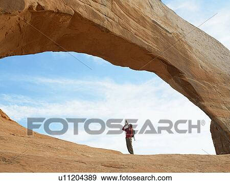 Stock Photo - Young man playing bugle under arched rock. Fotosearch