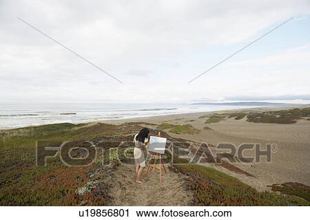 Stock Image - Young woman painting on beach. Fotosearch