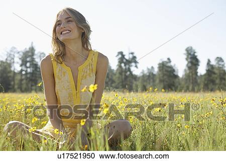 Stock Image - Young woman sitting in a field of wildflowers. Fotosearch