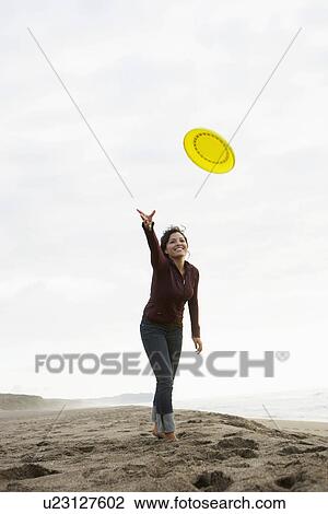 Stock Image - Young woman throwing frisbee on beach. Fotosearch