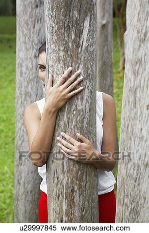 Stock Photography - Woman hiding behind tree. Fotosearch