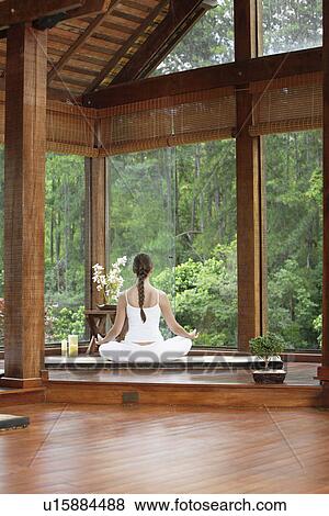 Stock Photo - Woman meditating on tatami near windows, rear view. Fotosearch