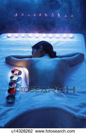 Stock Image - Young woman lying on towel near creams and candles. Fotosearch