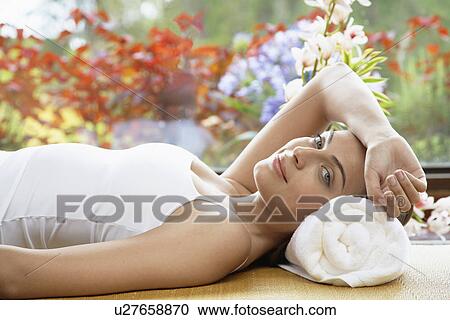 Stock Image - Young woman lying with head on rolled towel, portrait. Fotosearch