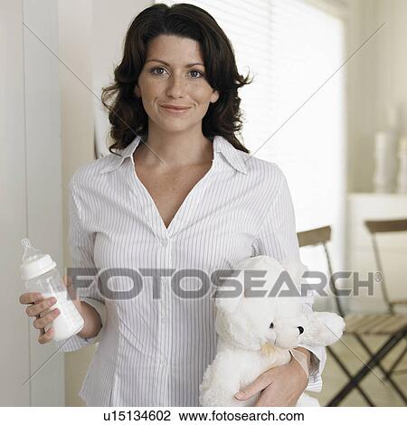 Stock Image - Woman carrying baby bottle and teddy bear. Fotosearch