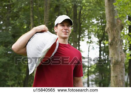 Stock Photography - Young man carrying sack on shoulder (low angle view). Fotosearch