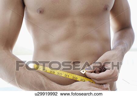 Stock Image - Young man measuring waist (midsection). Fotosearch