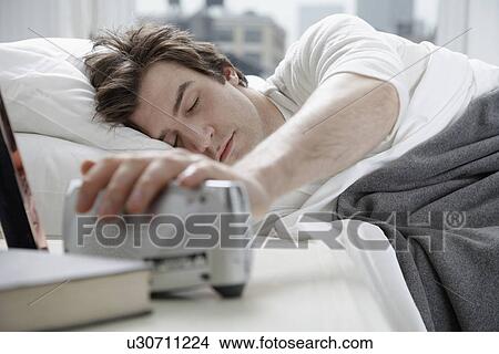 Young man switching alarm clock off View Large Photo Image Picture - Young man switching alarm clock off. Fotosearch