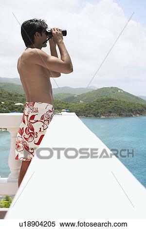 Stock Photography - Young man using binoculars at seaside, St. John, US Virgin Islands, USA. Fotosearch