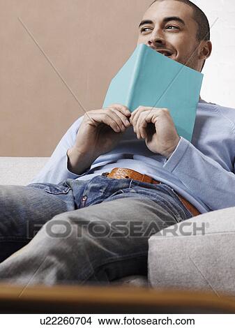 Picture - Young man with book on sofa. Fotosearch