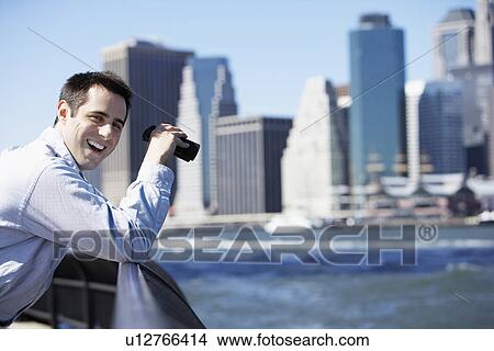Picture - Man using binoculars and laughing, Manhattan in background, New York City, New York, USA. Fotosearch