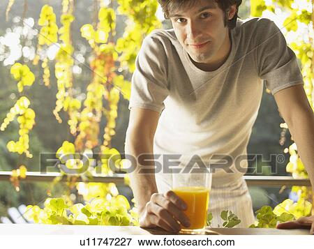 Stock Photo - Young man holding glass of orange juice (portrait). Fotosearch